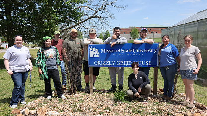The Agriculture Club stands by the blue Grizzly Greenhouse sign