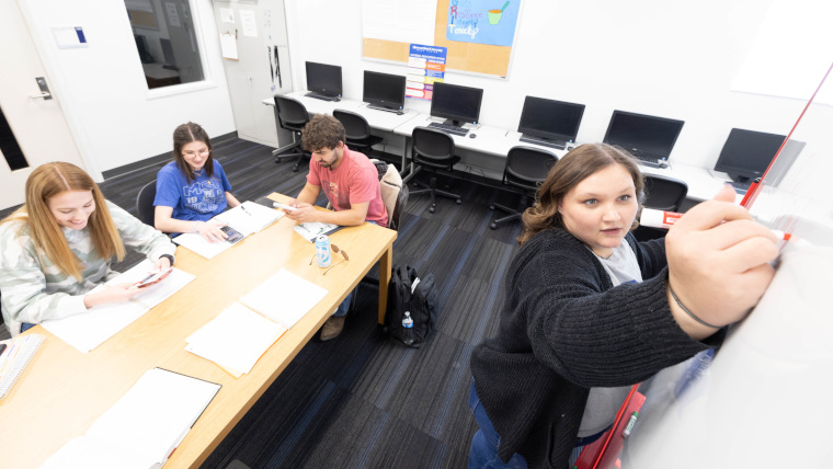 tutor writing on a white board helping 3 other students