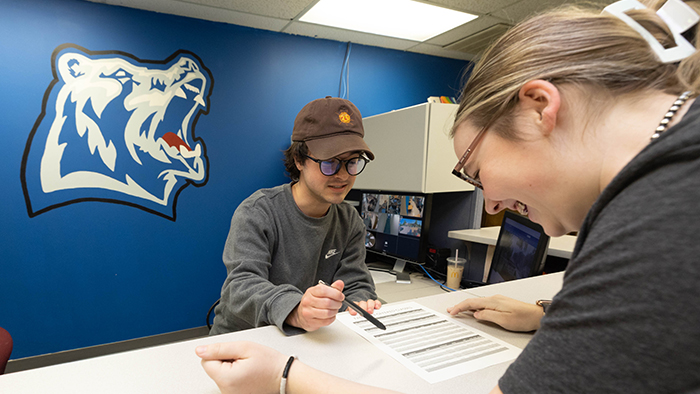 A front desk worker assists a student with the MSU-West Plains logo in the background