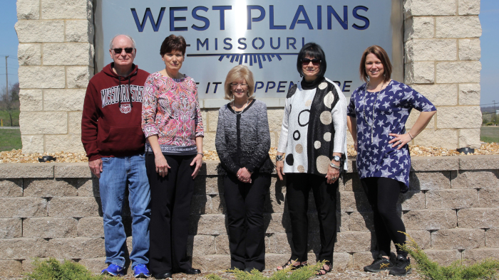 Five individuals in front of West Plains sign