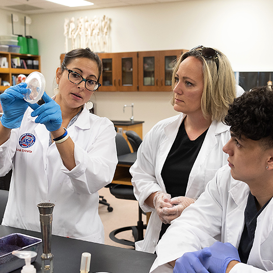 A professor works with two college students in a science lab