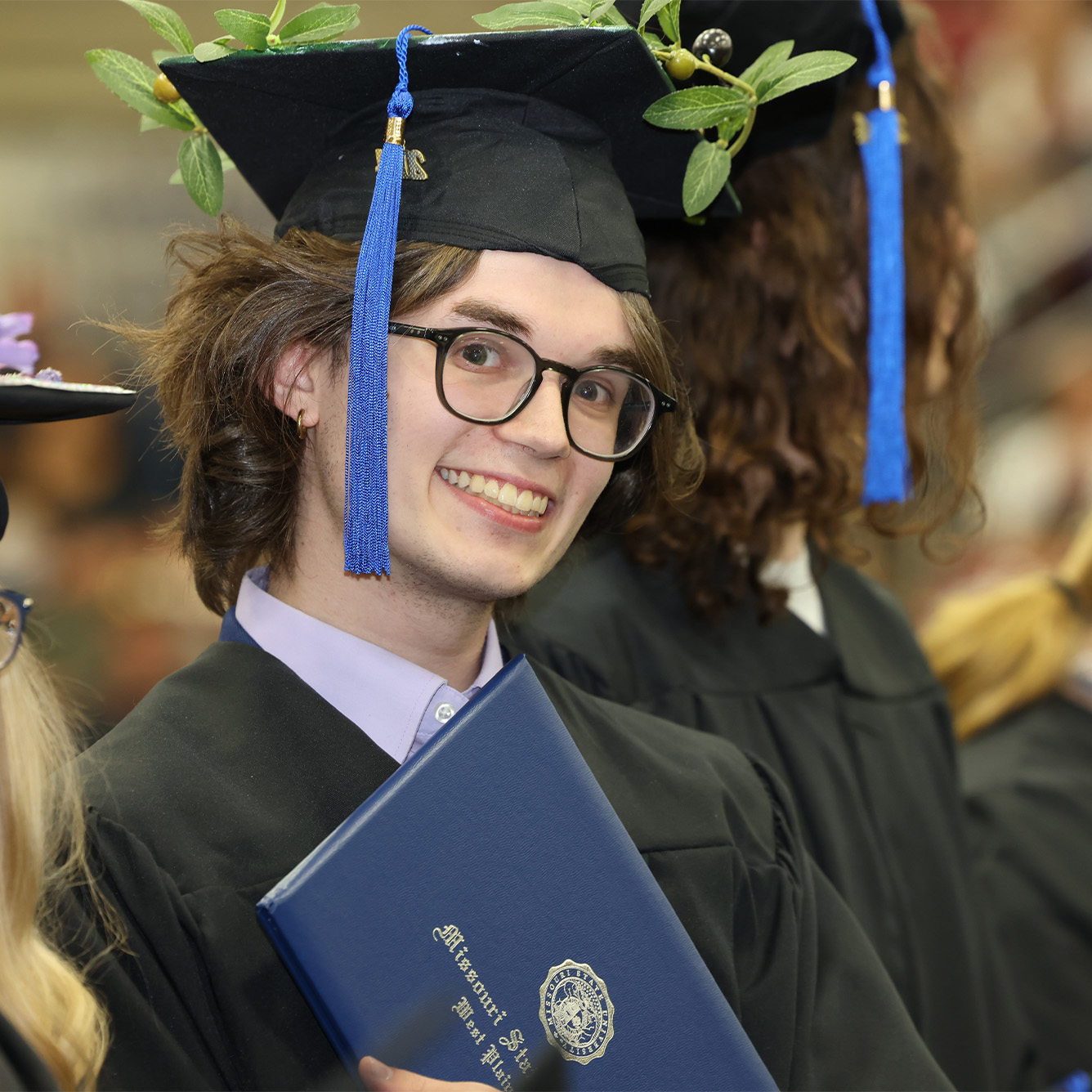 A graduate poses smiling with his degree cover in his cap and gown