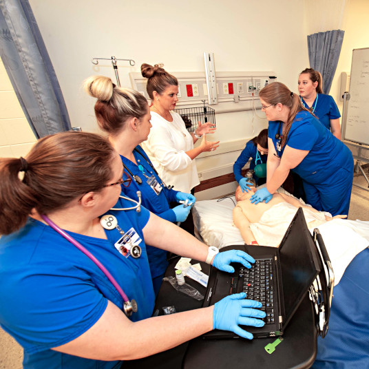 Nursing students stand around simulated hospital bed in lab