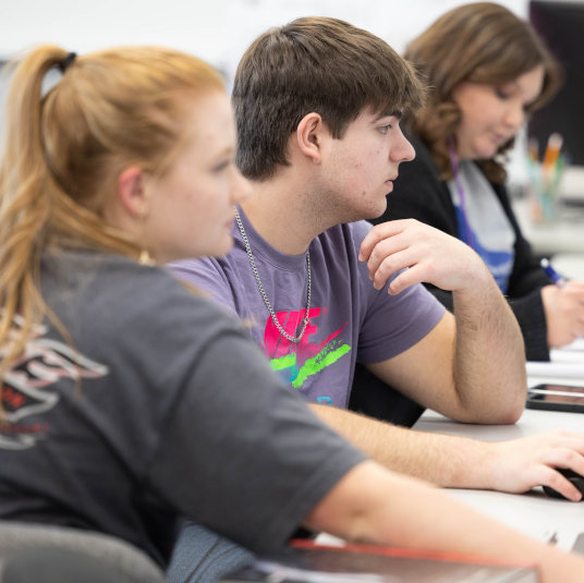 Three students look straight ahead at computers