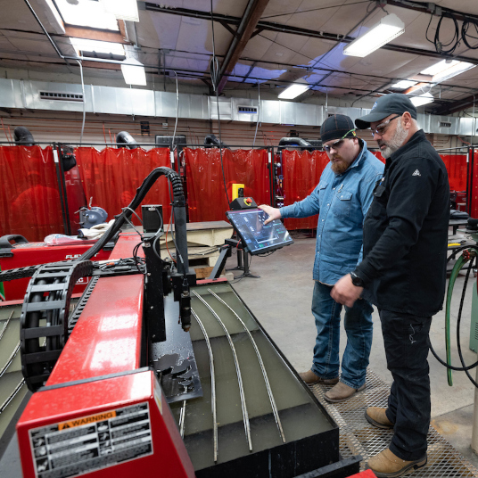 Welding instructor working with a student surrounded by various technology equipment 