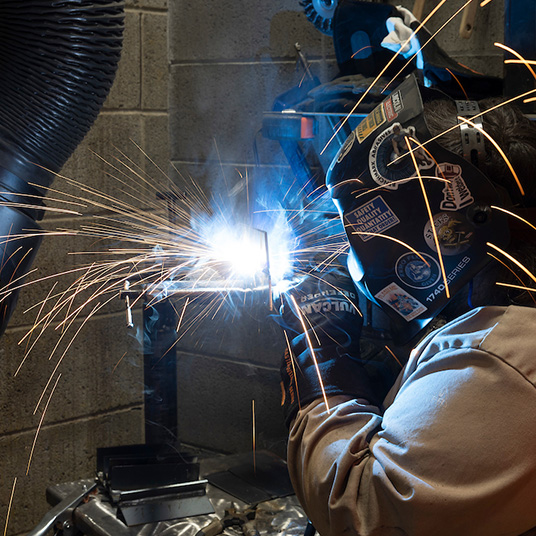 Welding student works on project in welding gear with sparks flying
