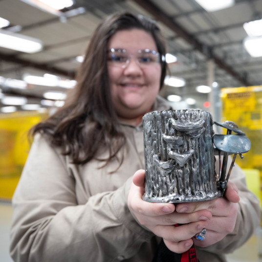 A female welding student wearing safety glasses shows off her welding project